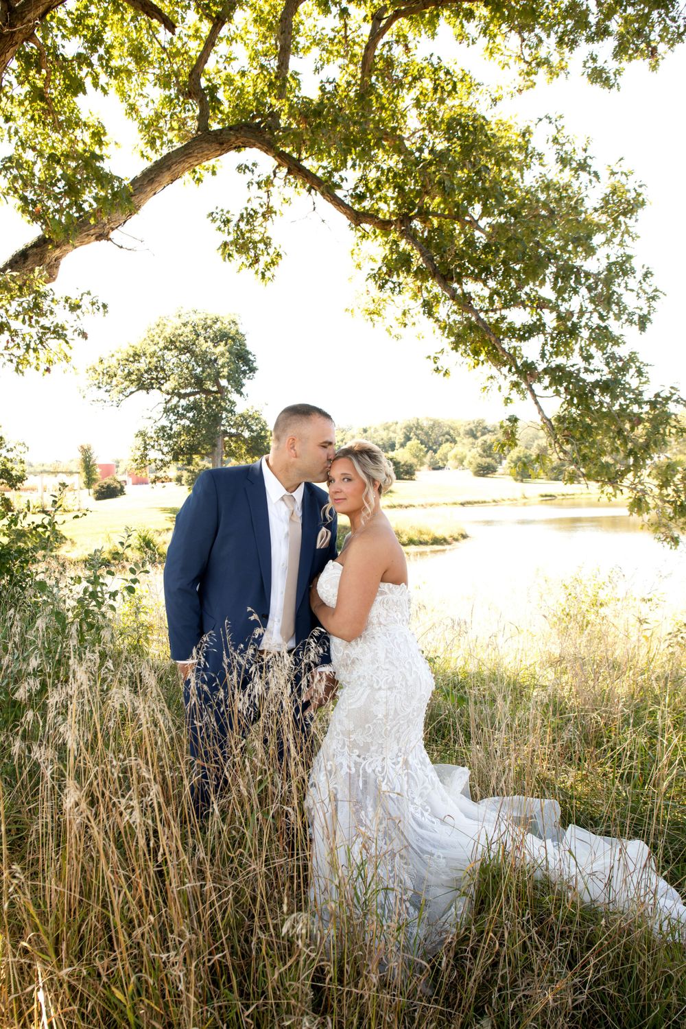 Romantic wedding portrait of couple in tall grass with lake and trees in background.