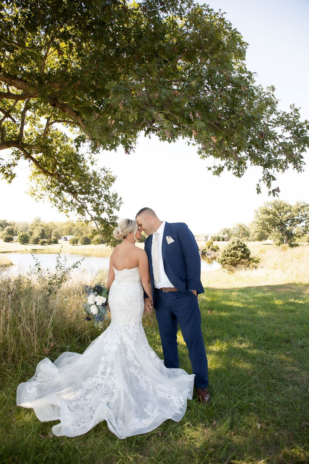 A strapless lace wedding gown with flowing train photographed outdoors near a pond.