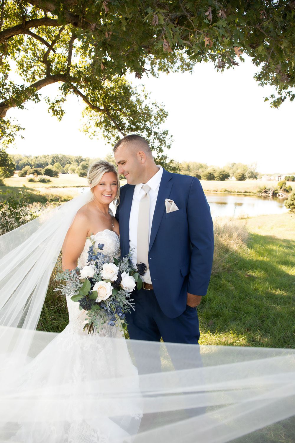 An elegant wedding photo featuring a flowing veil and blue and white bouquet in natural lighting.