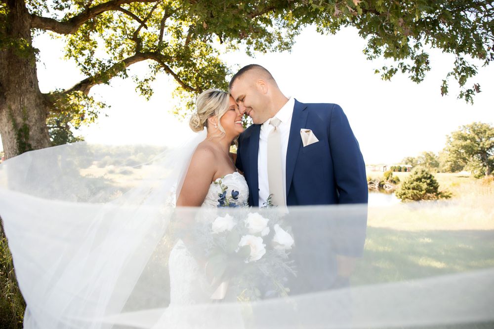 A romantic wedding moment captured under tree branches with flowing white veil.