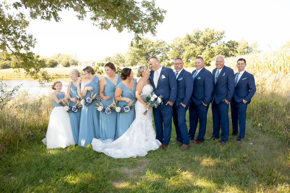 Wedding party in navy suits and light blue dresses poses together outdoors.