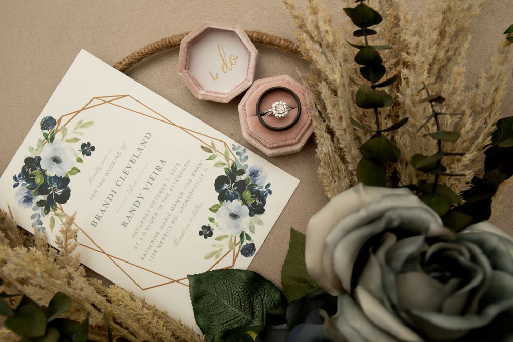 Wedding invitation with floral design displayed with rings in pink velvet box and roses.