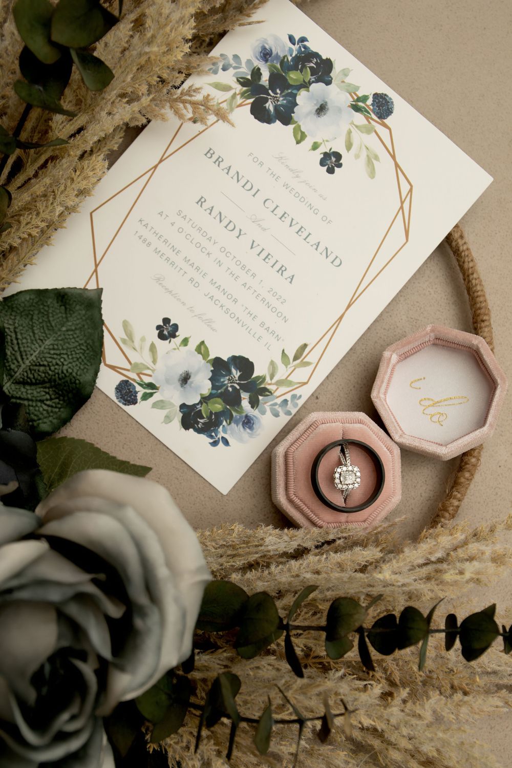 Elegant wedding invitation with blue floral design and geometric frame displayed with ring box.