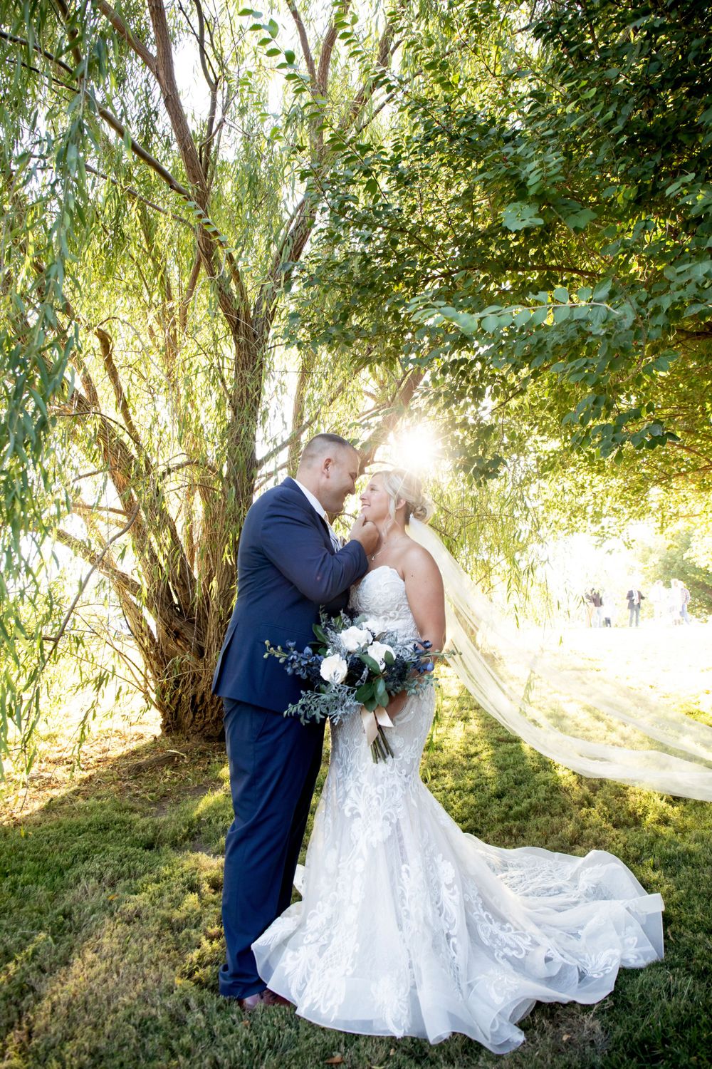 A romantic wedding portrait with sunlight streaming through willow trees.