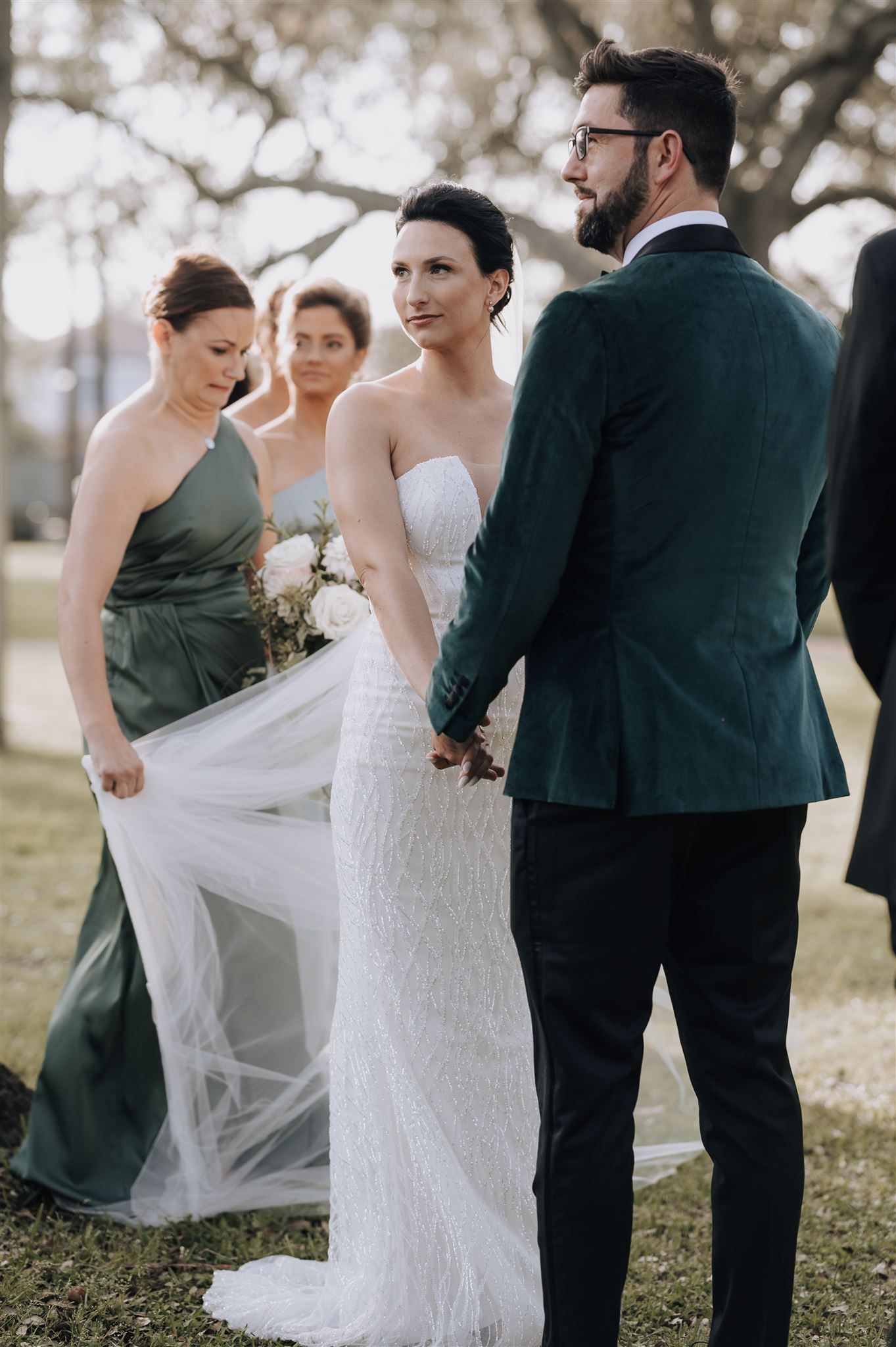 Bridal party members help adjust the wedding dress train during outdoor ceremony.