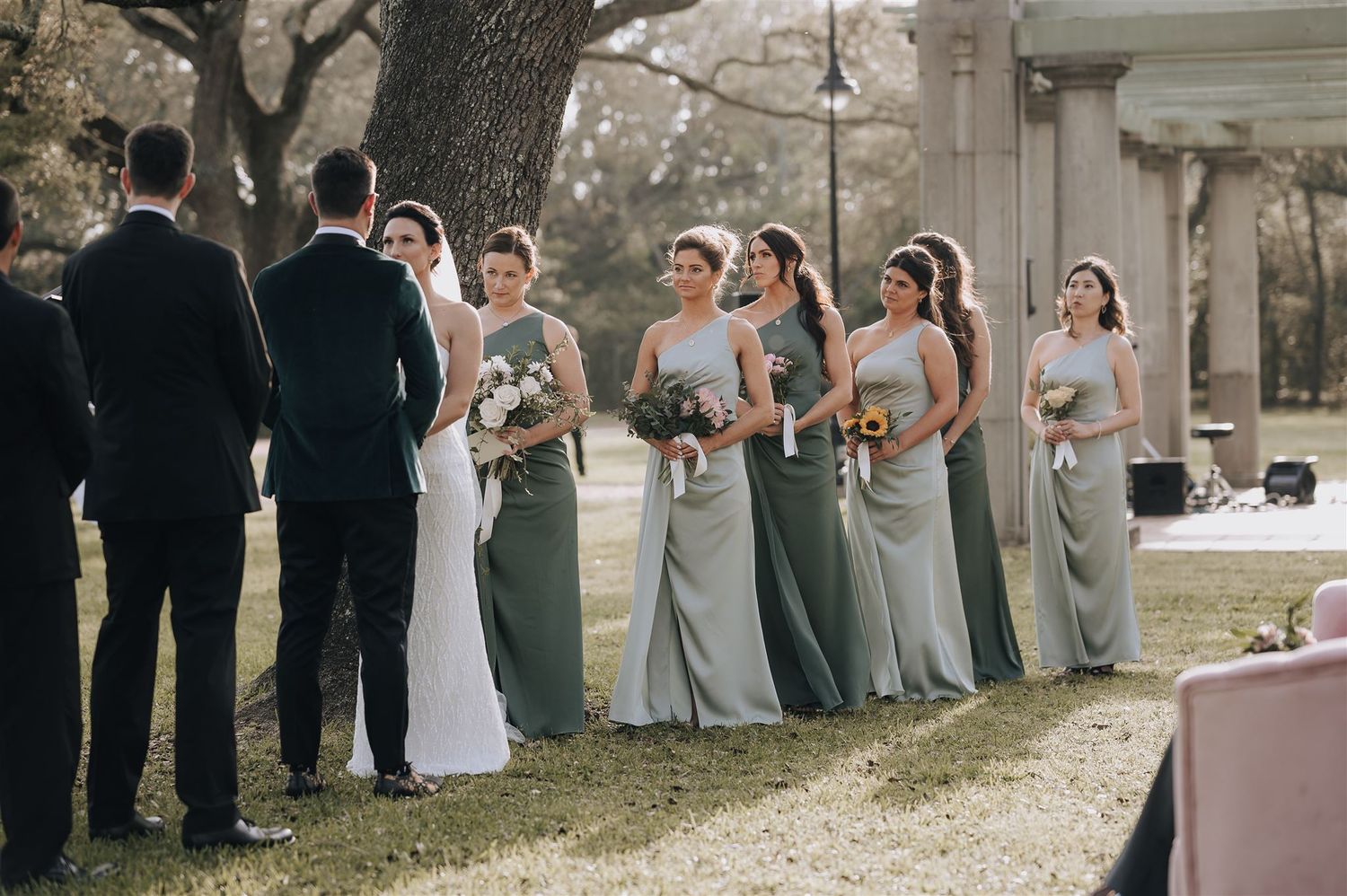 Wedding party lined up during outdoor ceremony with bridesmaids in sage green dresses.