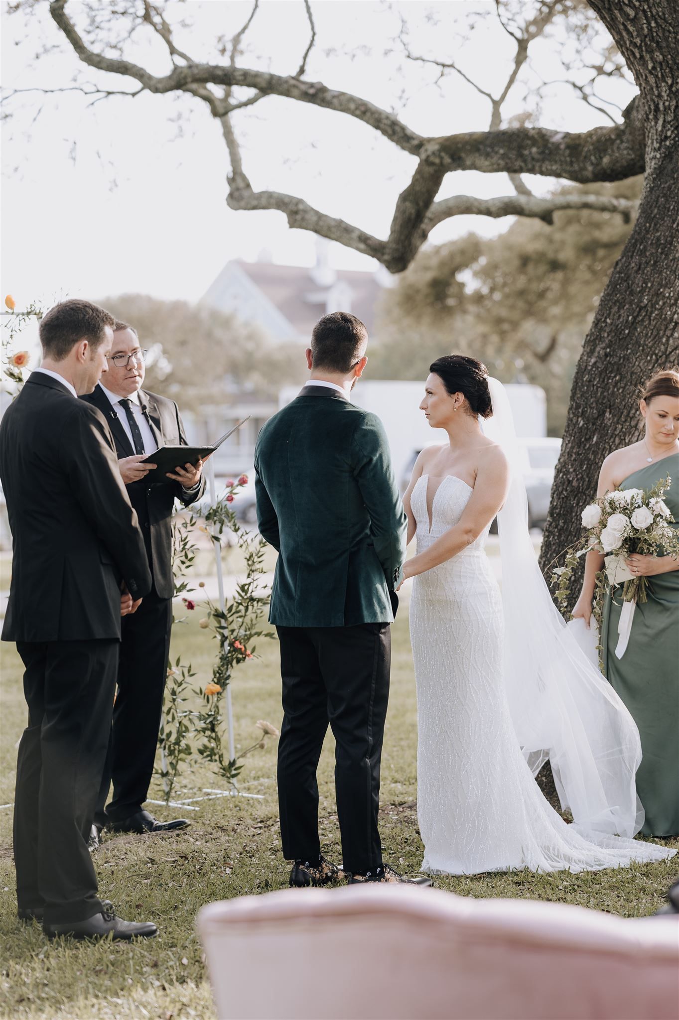 Wedding ceremony under a large tree branch with officiant leading the service.