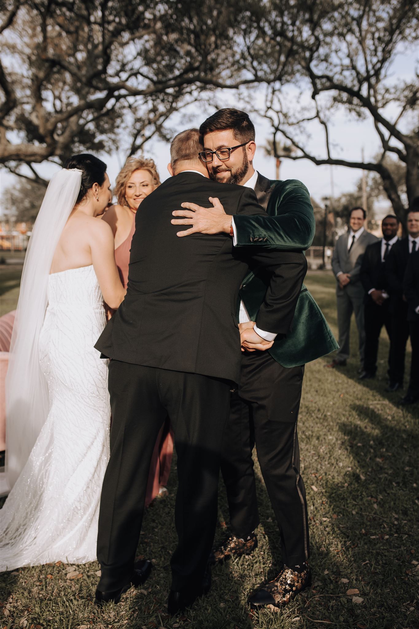 Emotional embraces shared during outdoor wedding ceremony beneath ancient oak trees.