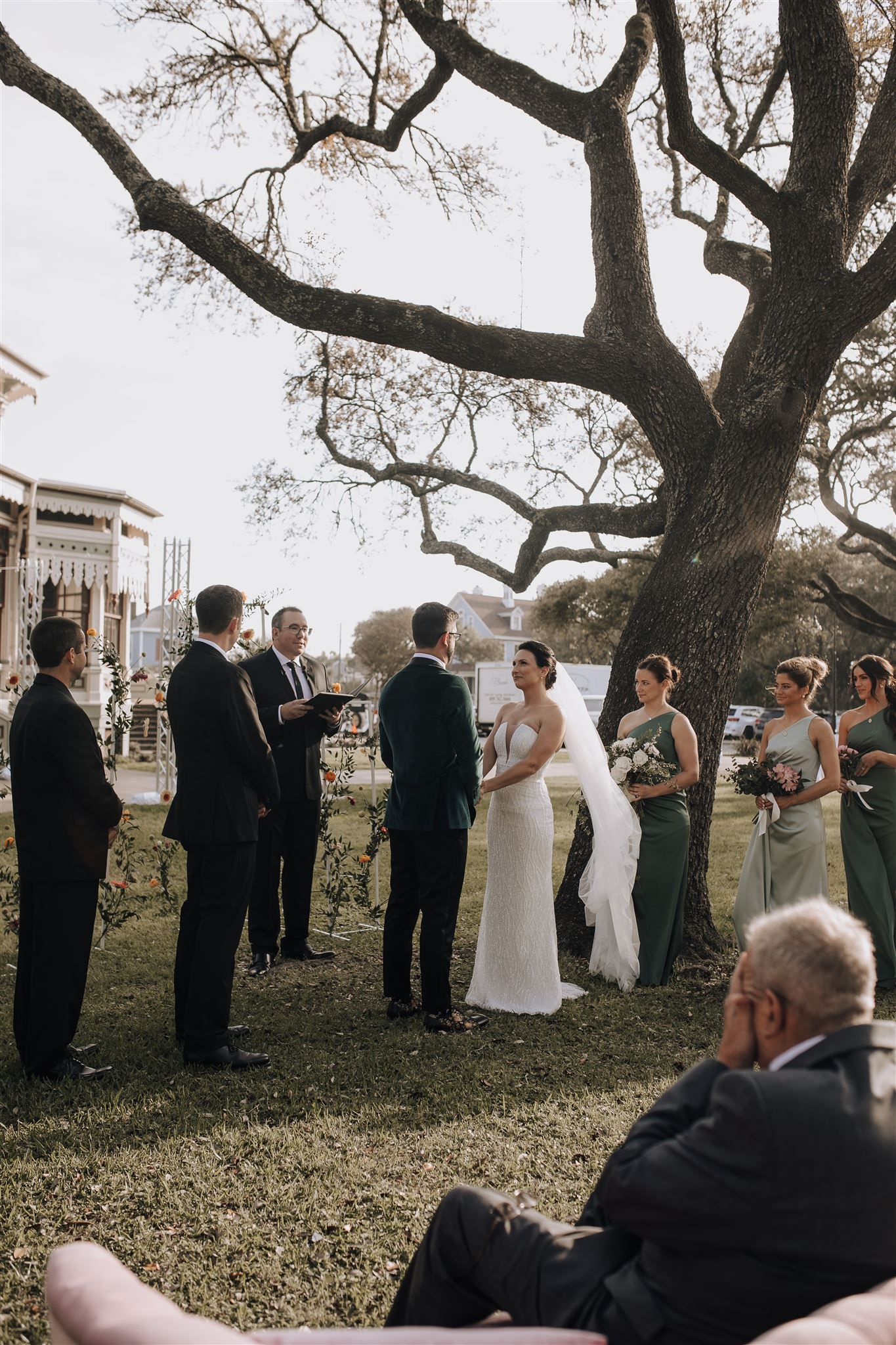 Wedding party gathered under a majestic old tree during an outdoor ceremony.