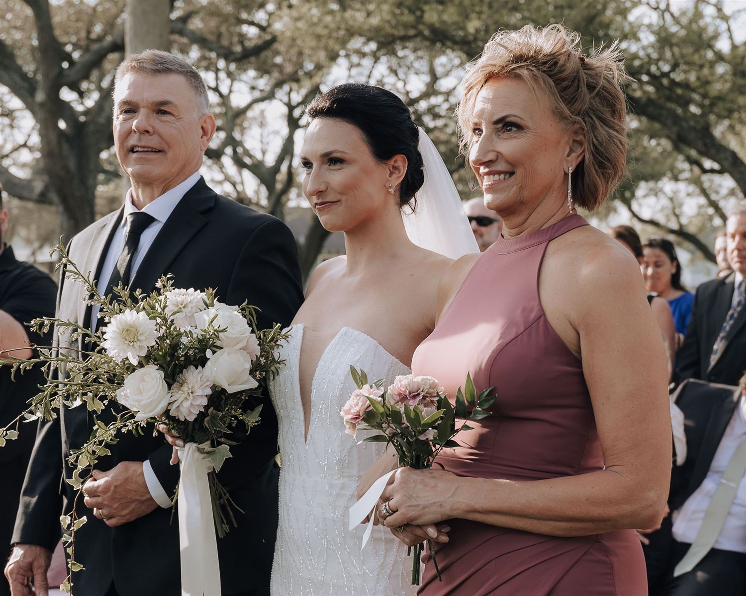 Wedding party members holding white floral bouquets during outdoor ceremony.