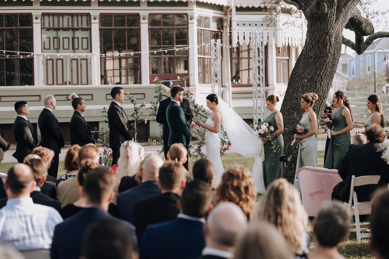Outdoor wedding ceremony at historic venue with guests watching from white chairs.