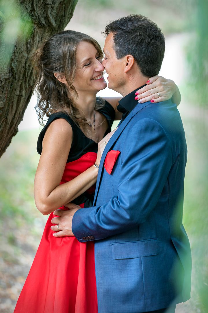 Couple in formal attire sharing an intimate moment near a tree.