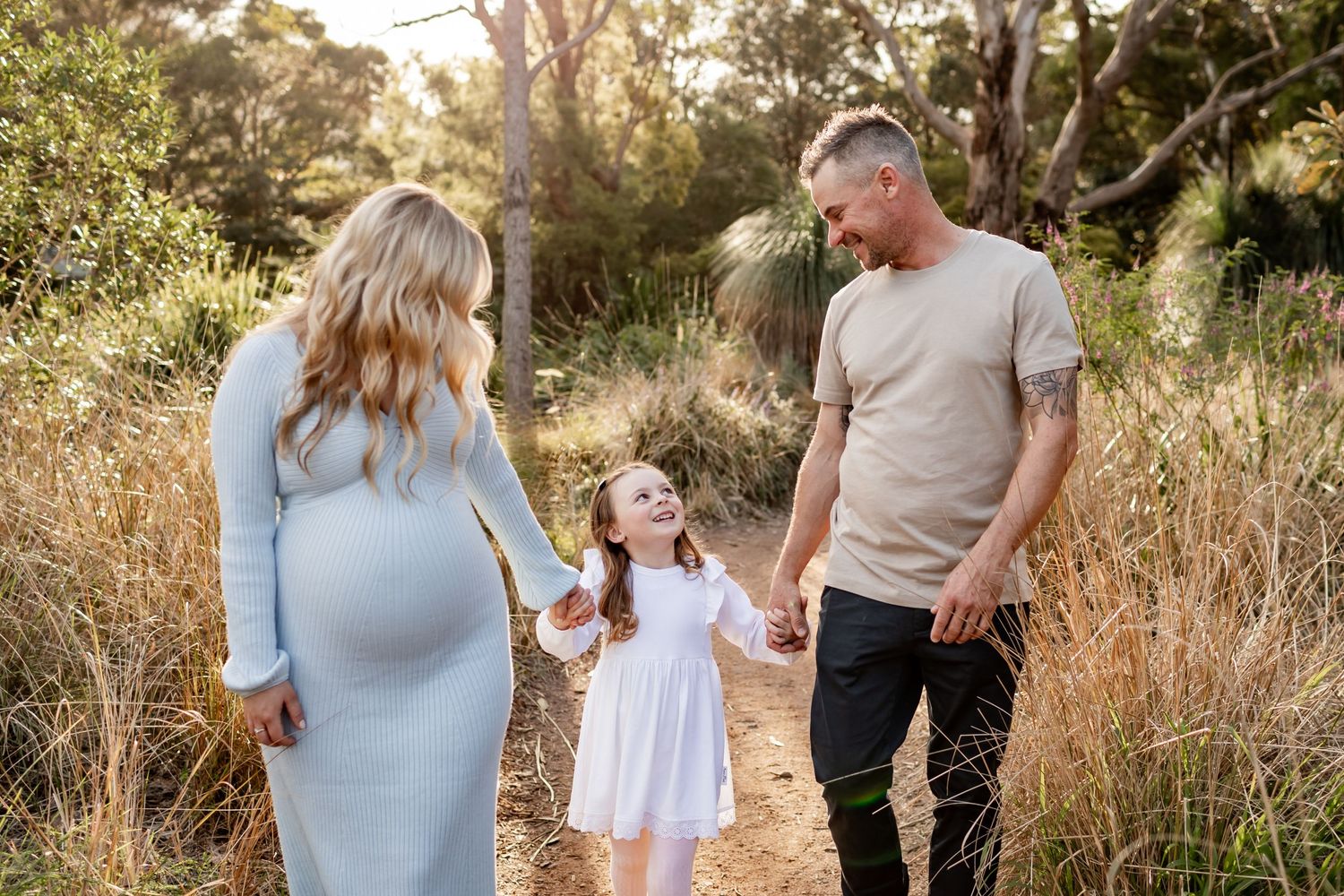 Family walks hand in hand along scenic bush trail during golden hour.
