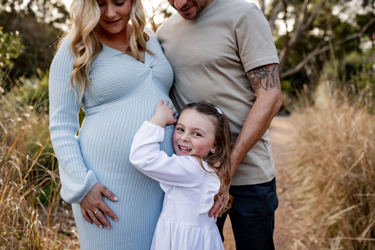 Family poses together on nature trail with young girl hugging pregnant mother.