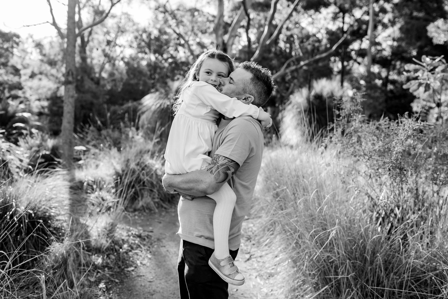 Black and white capture of father and daughter embracing on nature trail.