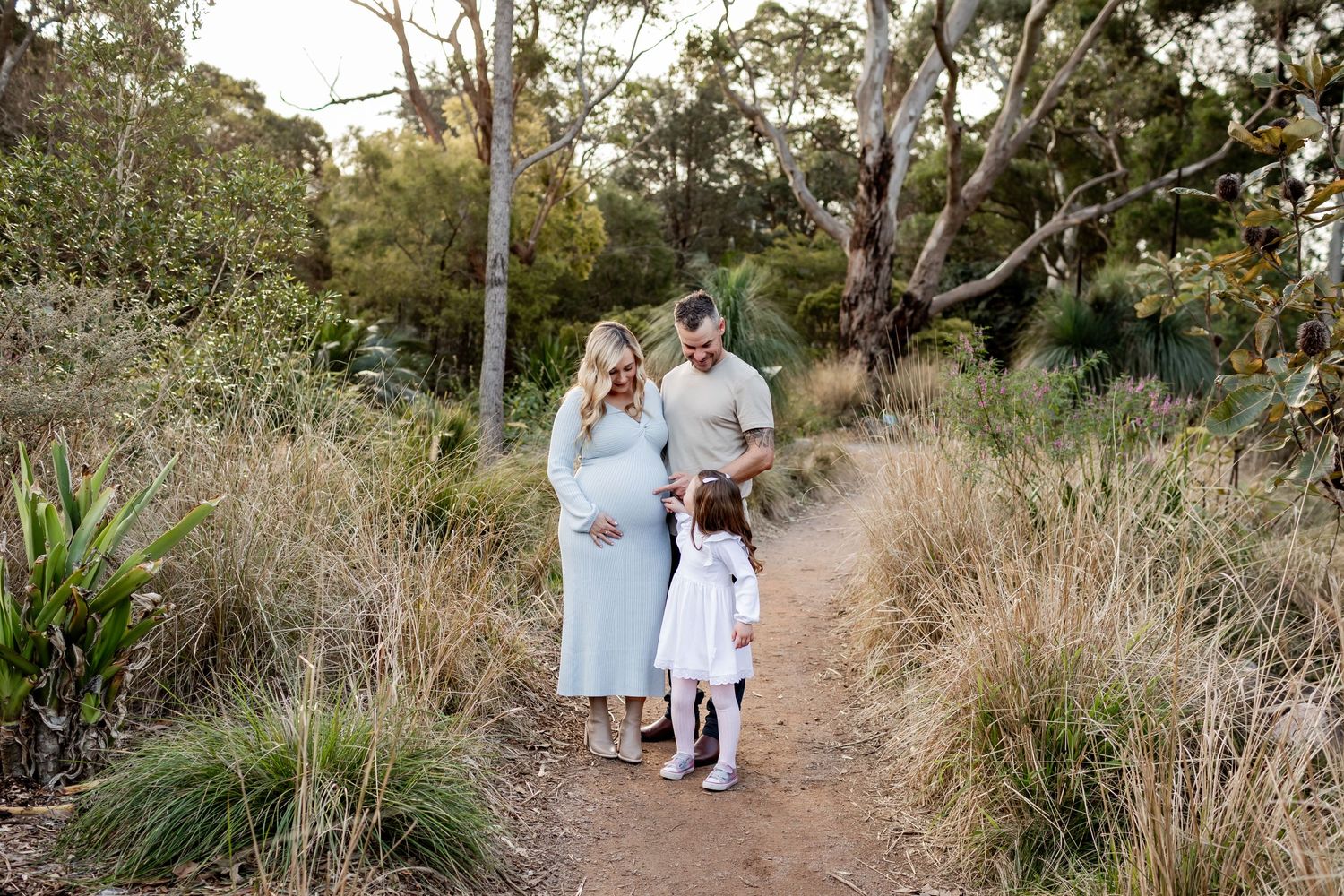 Family takes a stroll together on dirt path through scenic bushland.