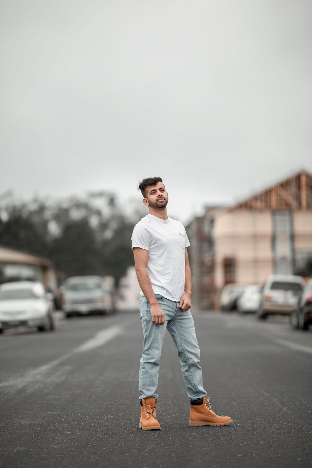 Person in casual white t-shirt and light jeans standing on street with tan boots and urban background.
