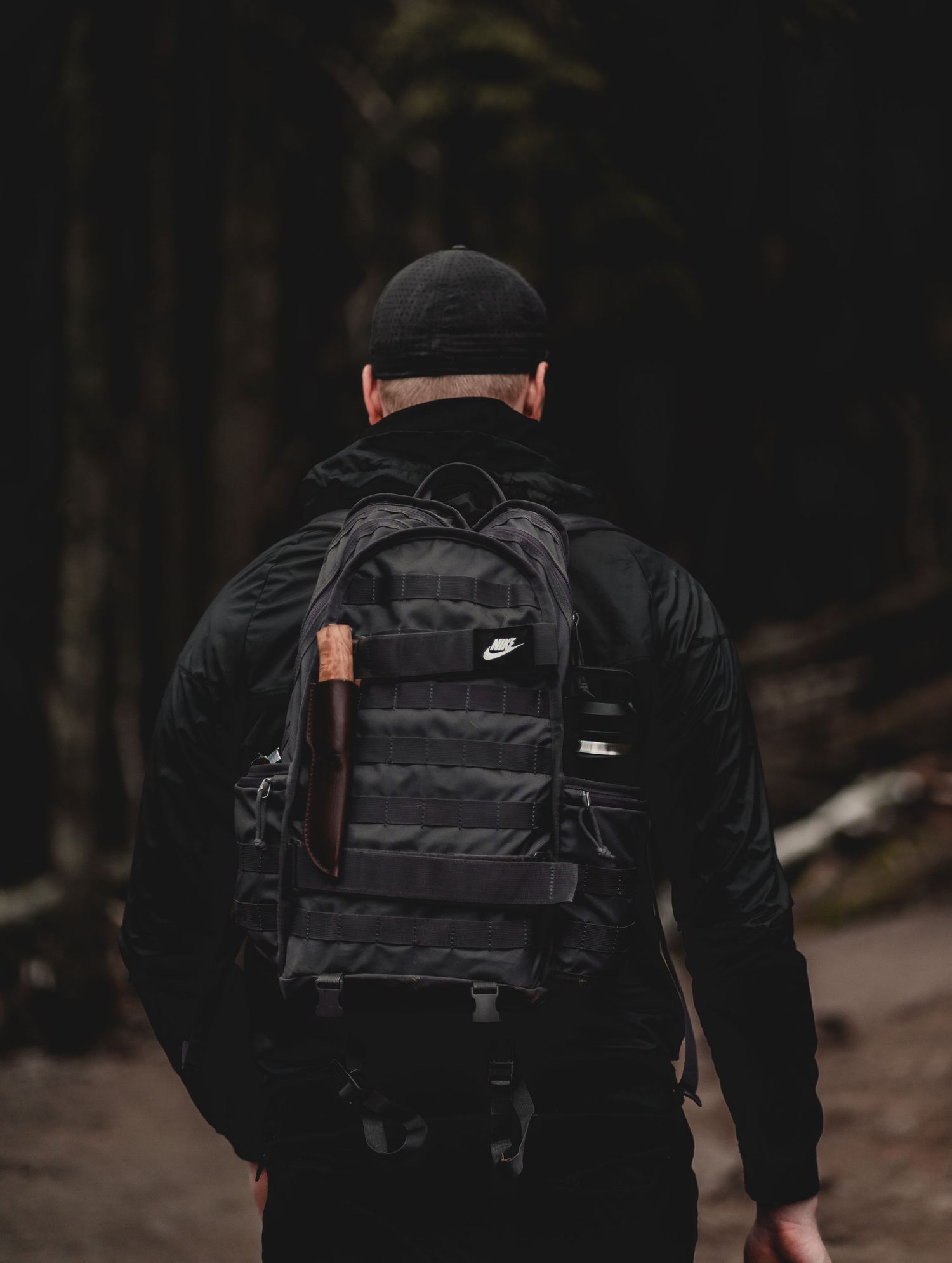 Person wearing black clothing and backpack walking through dark forest path.
