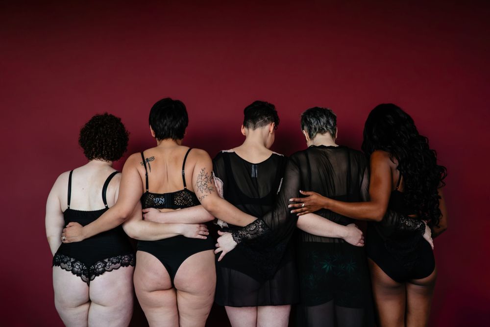 Seven figures in dark outfits stand against a maroon background showing different poses.