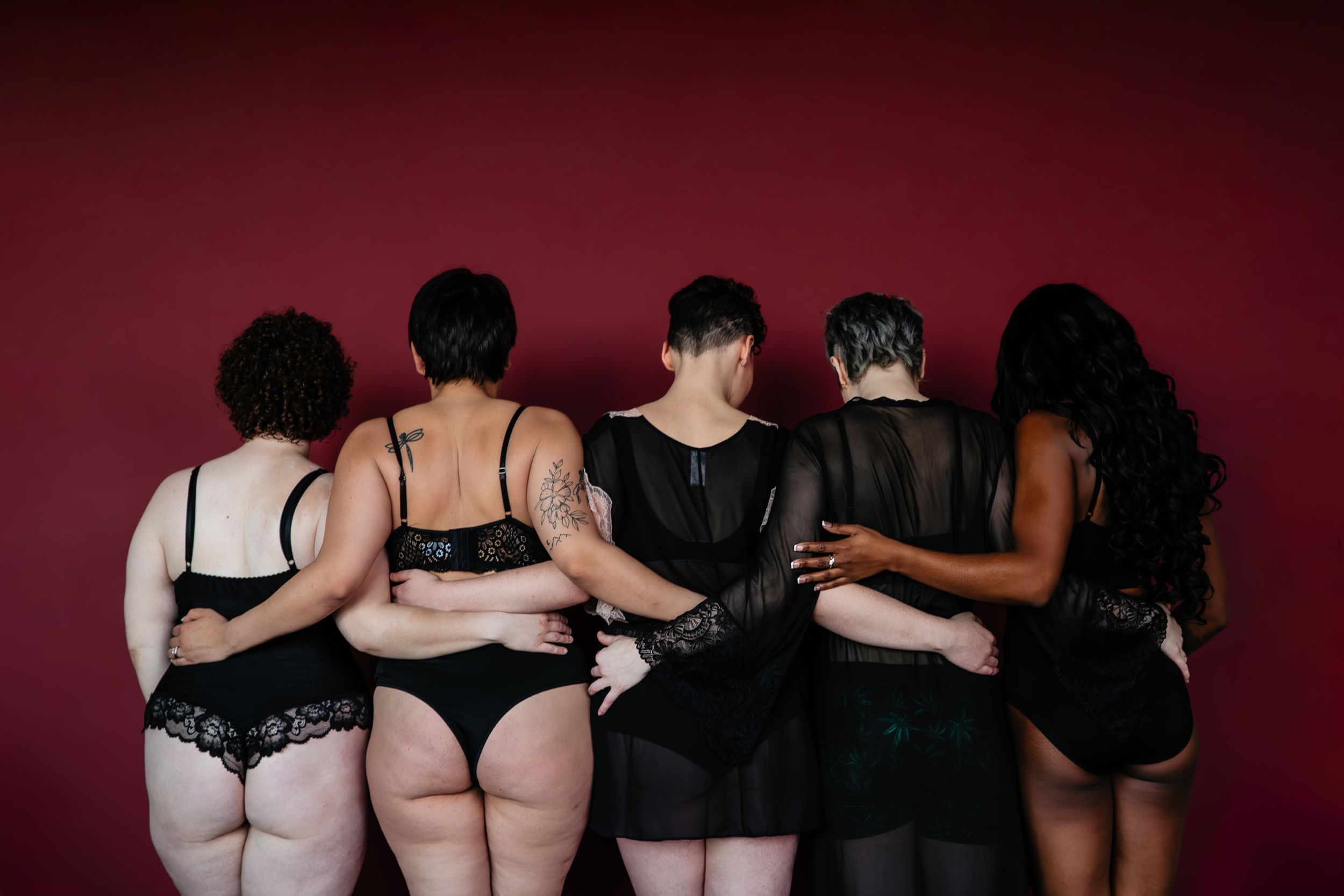 Seven figures in dark outfits stand against a maroon background showing different poses.