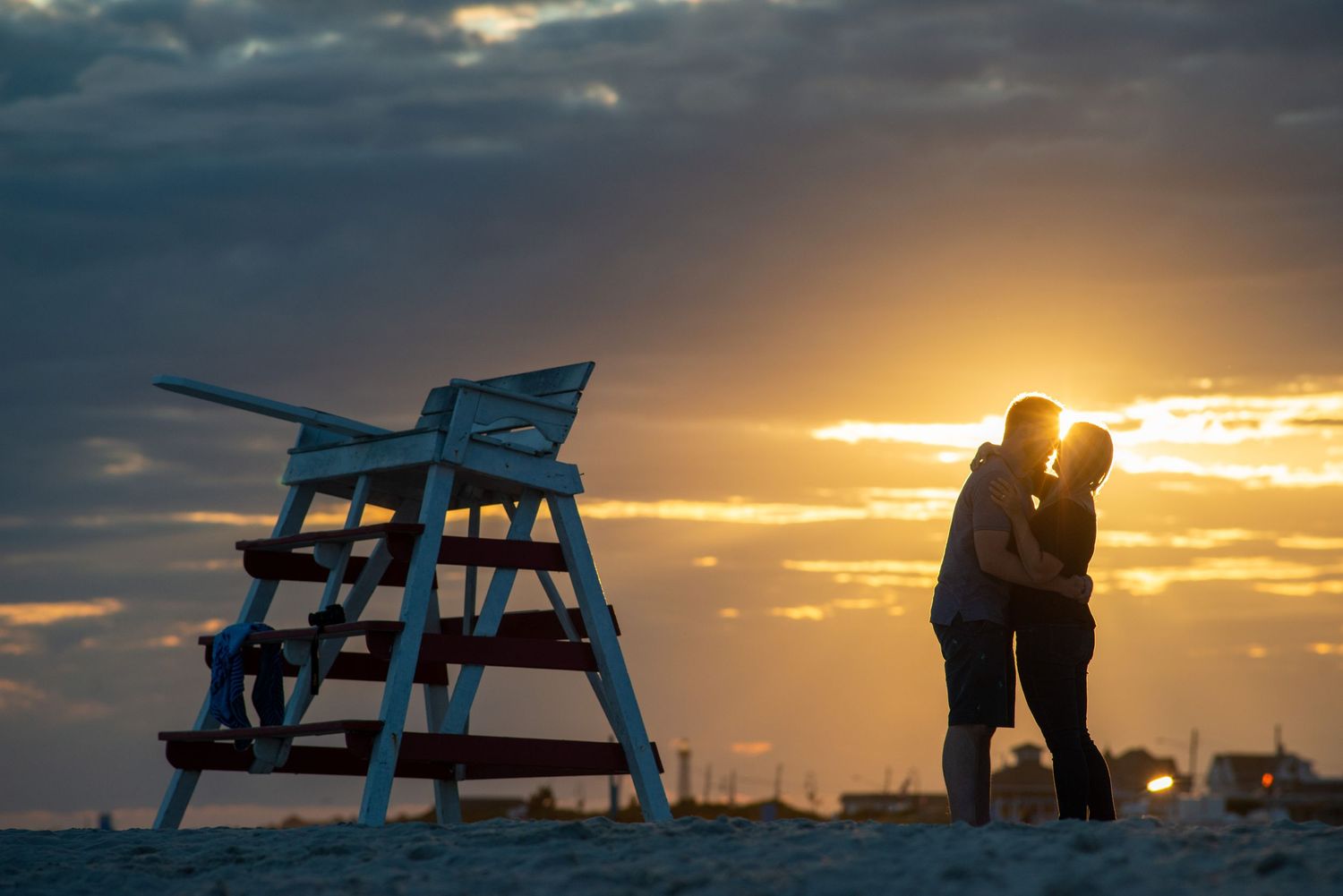 A romantic beach scene at sunset with a lifeguard chair silhouetted against the golden sky.