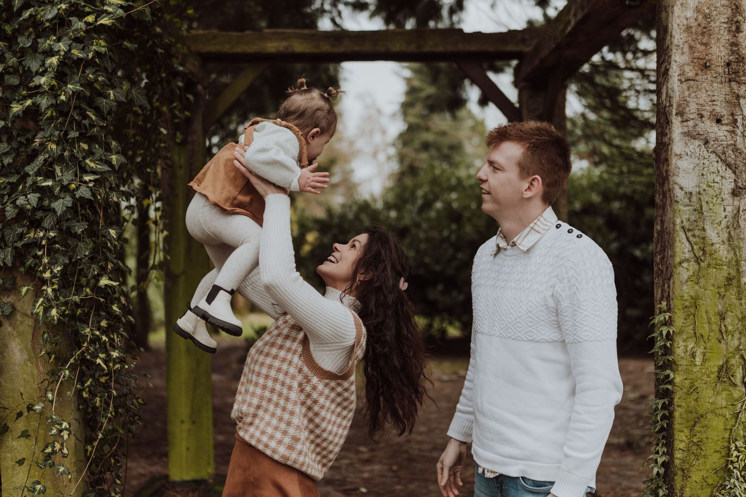 A young family shares a playful moment together under a wooden archway.