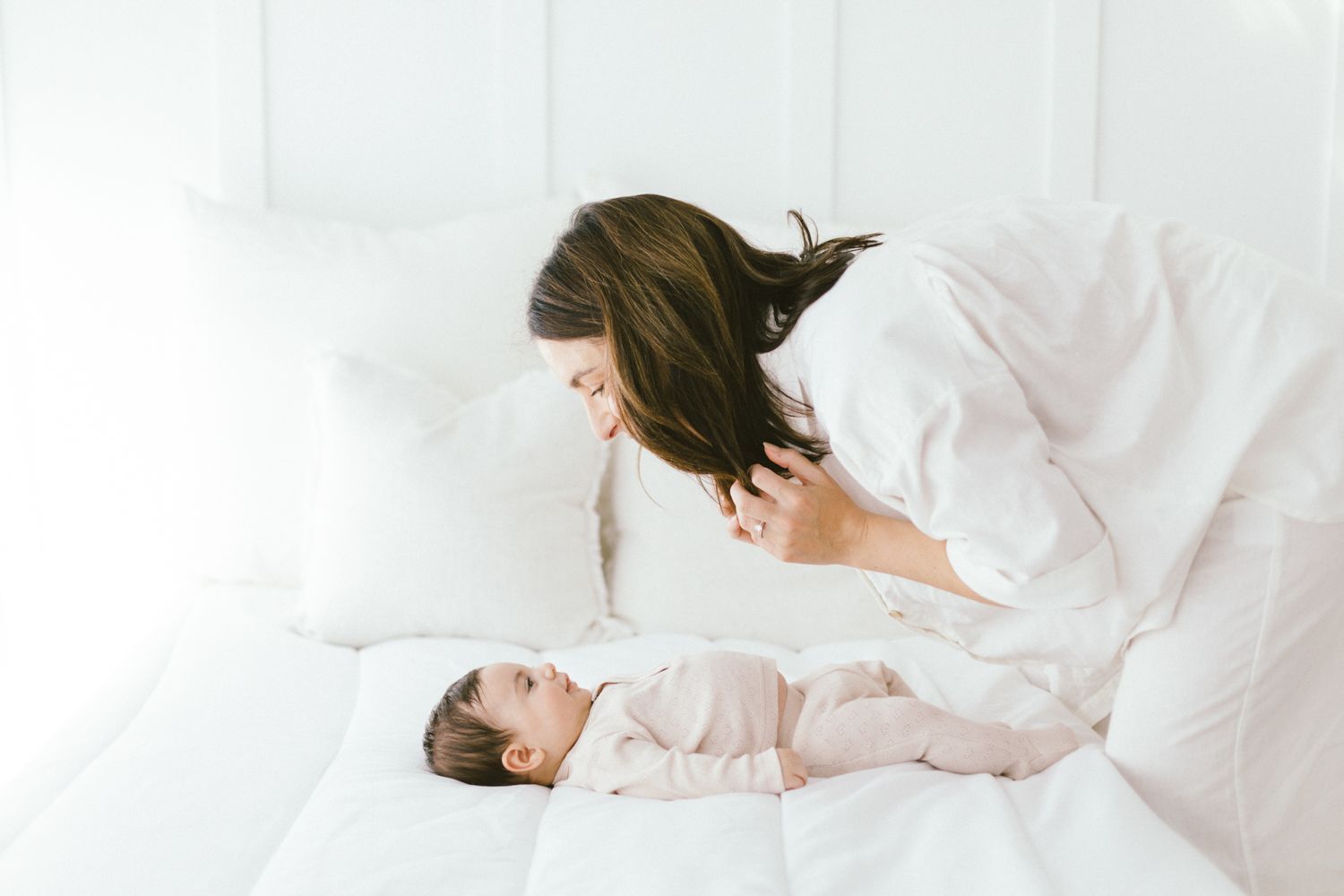 Loving interaction between caregiver and infant on white sheets.
