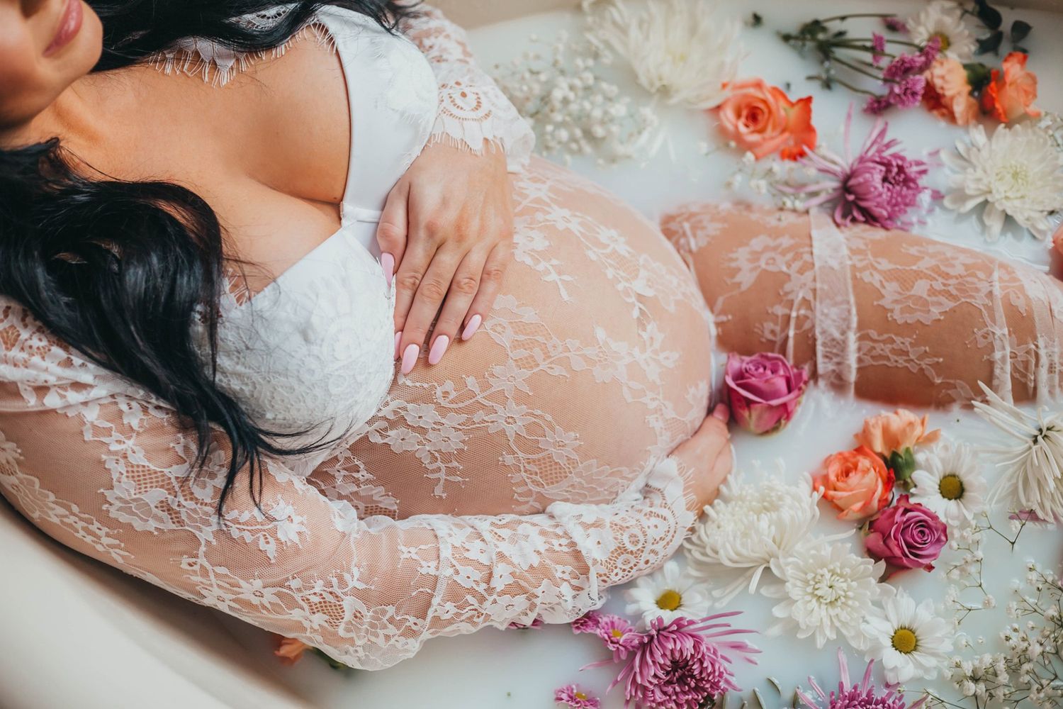Intimate maternity photo with lace overlay and scattered fresh flowers.
