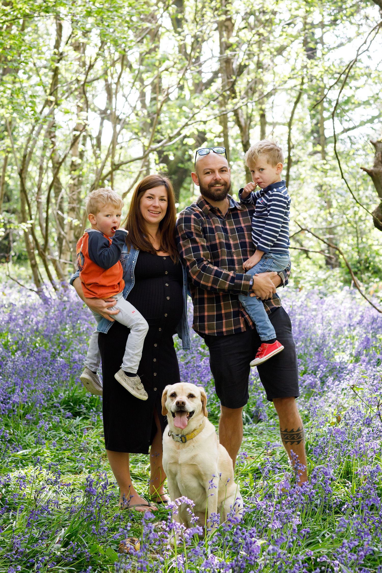 Happy family with dog posing in blooming bluebell woodland.