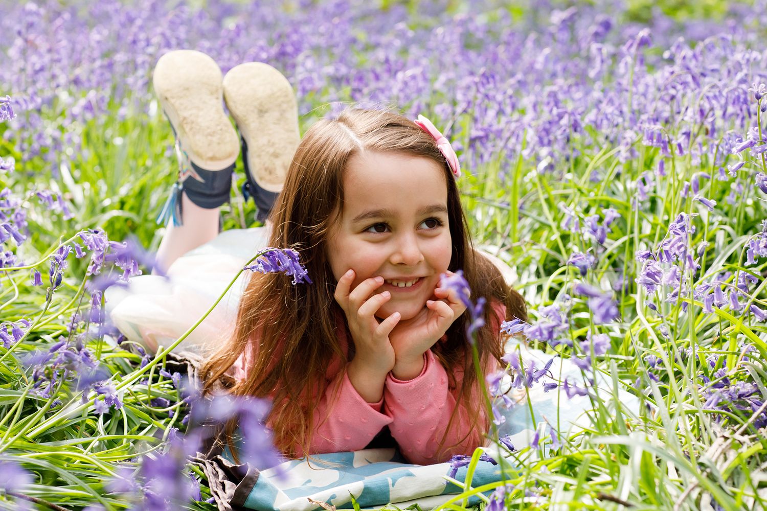 Young person lying among purple bluebells in spring woodland.