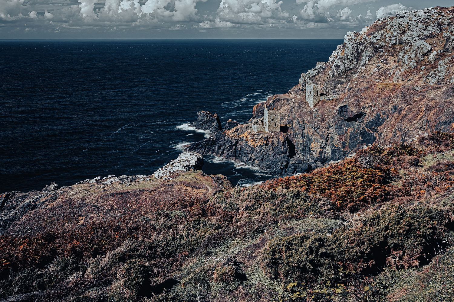 Dramatic coastal landscape with rocky cliffs overlooking deep blue ocean waters.