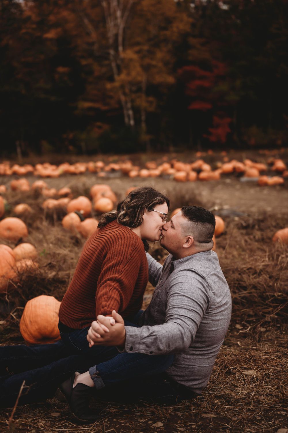 A romantic moment captured in a pumpkin field during fall with autumn colors in the background.
