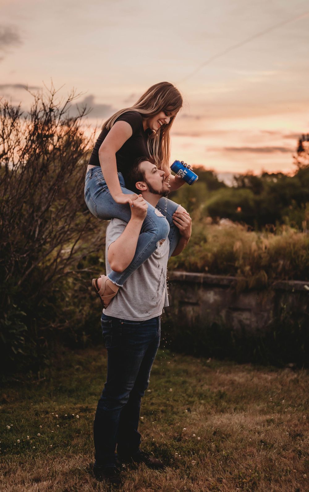 Playful couple shares piggyback ride at sunset in grassy field.