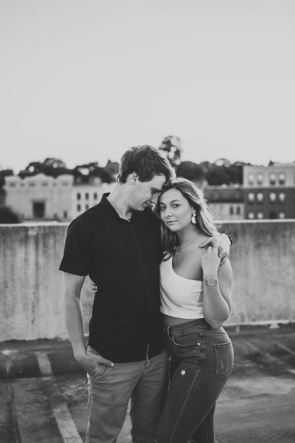 Romantic black and white portrait of a couple embracing on an urban rooftop at sunset.