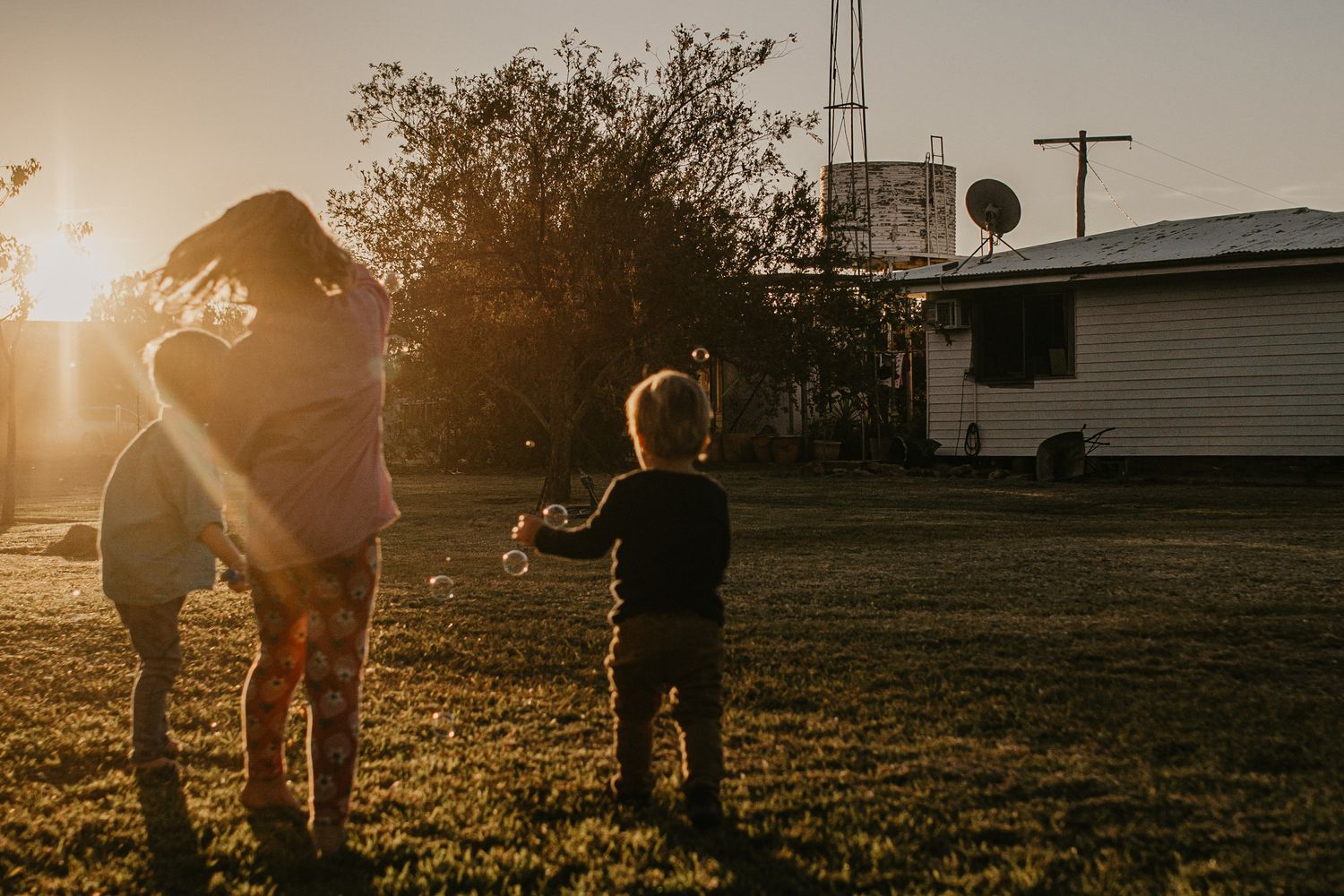 Kids at sunset in their backyard on their property blowing bubbles