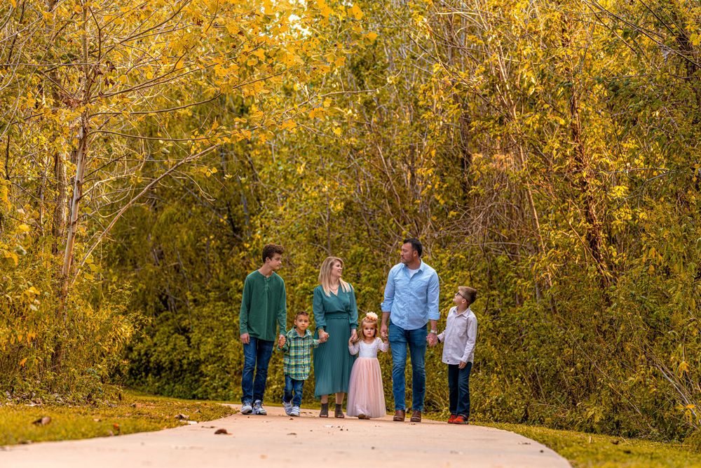 A family of five walks together on a path surrounded by golden autumn trees.
