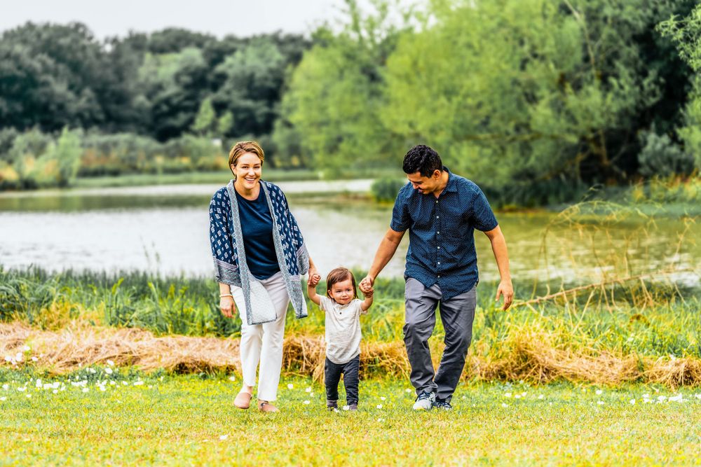 Family walking together and holding hands on grassy path near a lake.