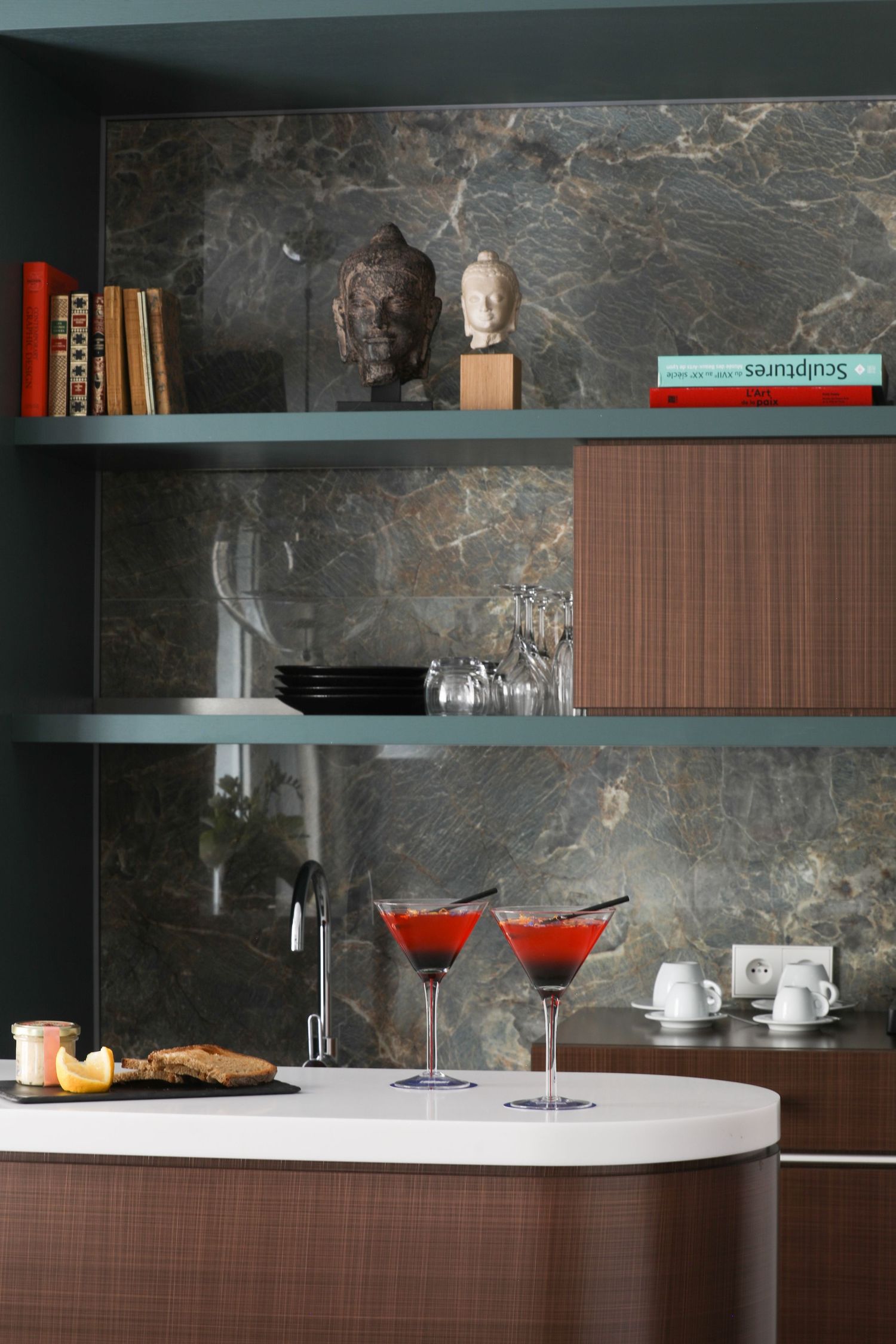 Modern bar shelf with marble backdrop, red cocktails and decorative busts on display.