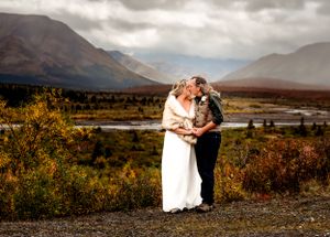 Wedding couple embracing on mountain path with scenic valley view.