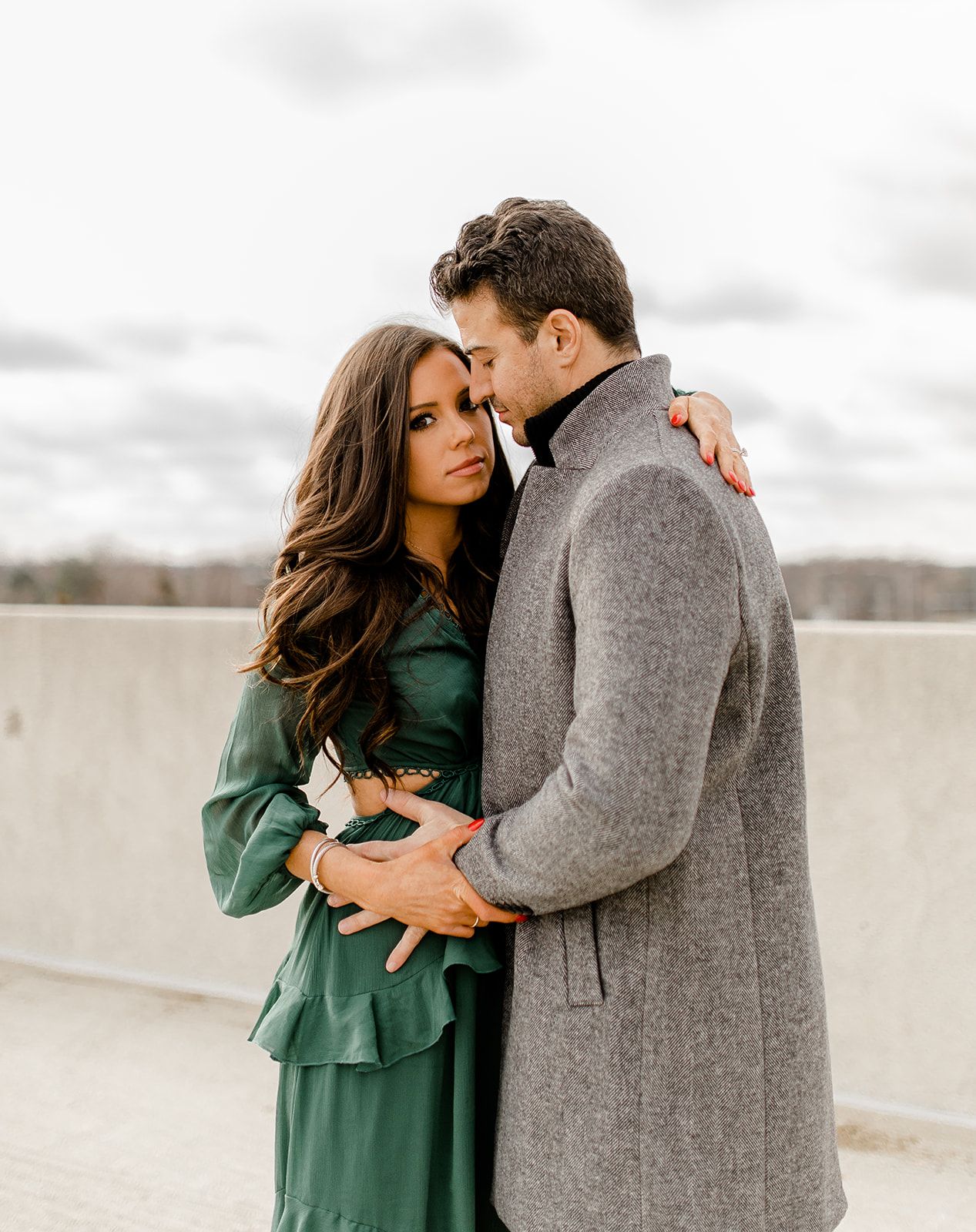 Intimate couple's portrait in winter coats against cloudy sky.