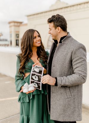 Couple sharing ultrasound photos while wearing winter coats on a rooftop, showing excitement about their pregnancy announcement.