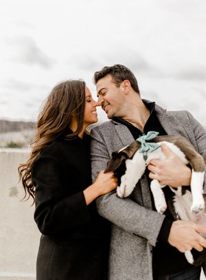 Intimate moment between couple in winter coats while holding their small dog on urban rooftop.