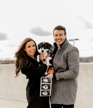 Happy couple holding their small dog and ultrasound photos during outdoor photoshoot.