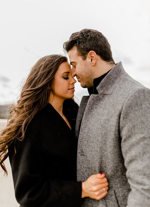 Intimate close-up of couple in winter coats sharing tender moment against cloudy sky.