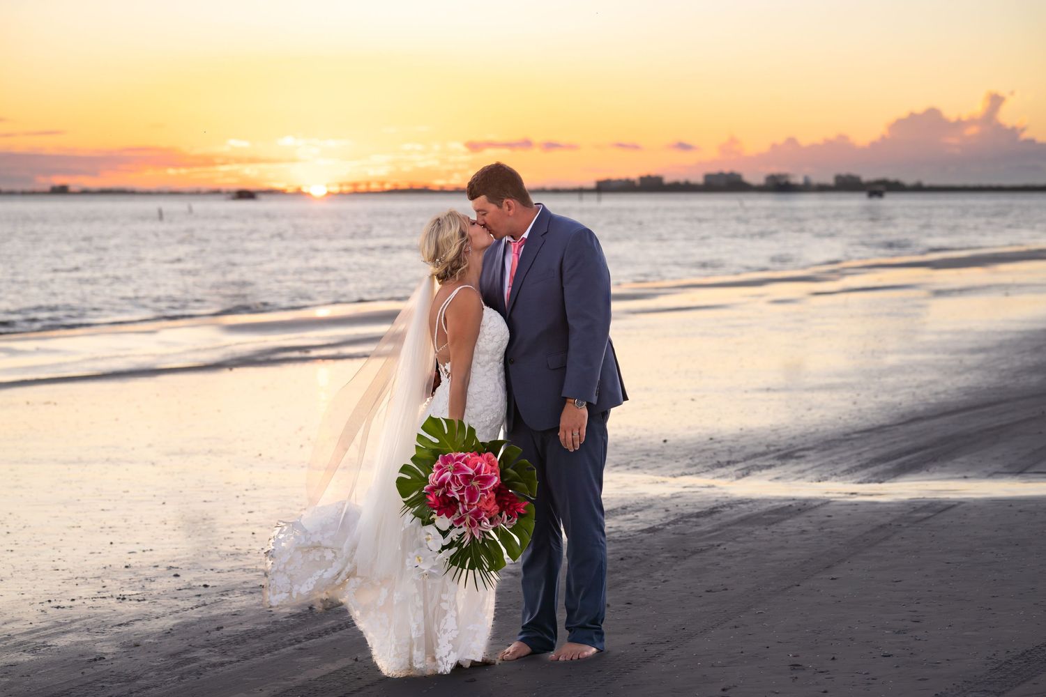 Beach wedding couple silhouetted against vibrant orange sunset.