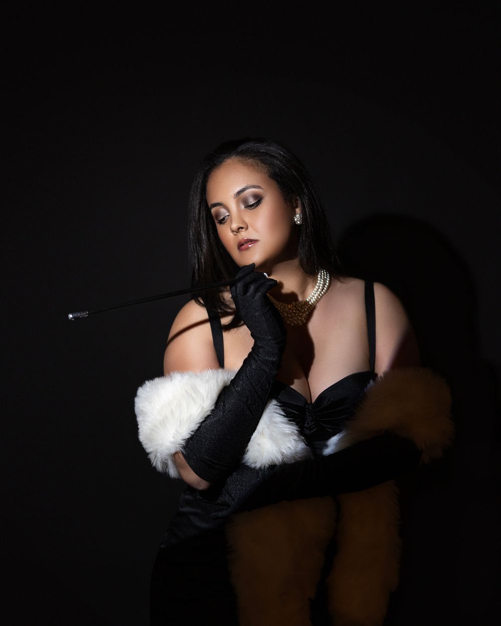Film noir inspired portrait with black gloves and white fur stole against dark background.