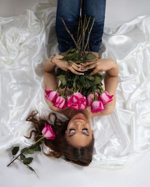 Creative overhead portrait with pink roses and white fabric showcases feminine styling.