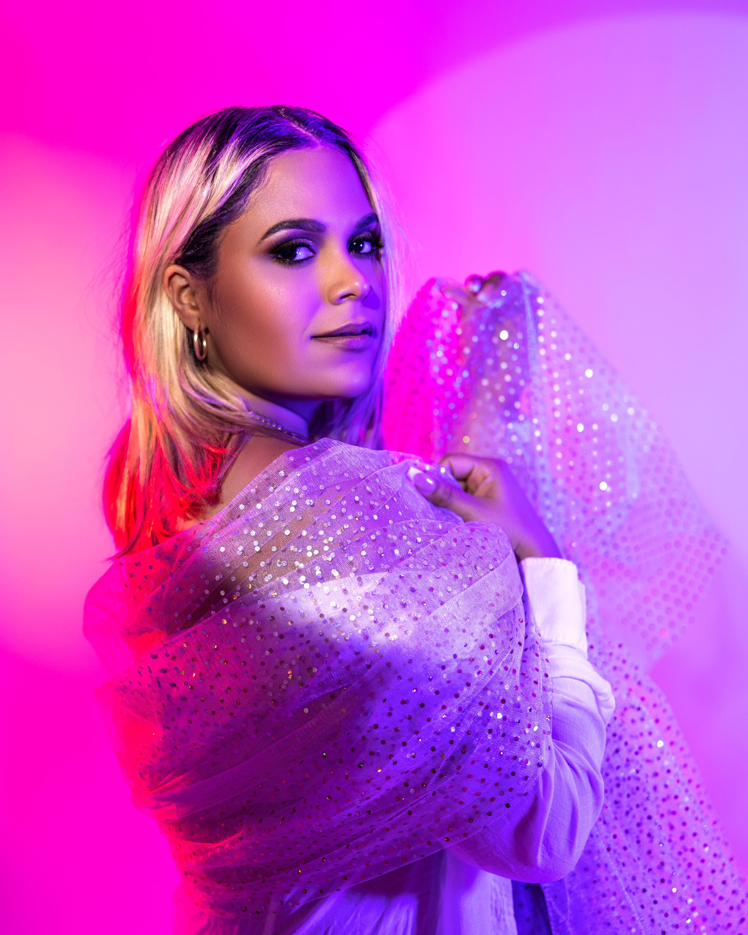 Glamorous fashion portrait with sparkly dress against vibrant pink and purple lighting.