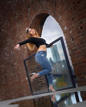 Dynamic pose on brick archway balcony in urban setting wearing casual attire.