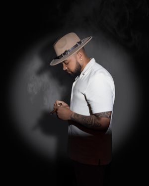 Moody portrait of person in white shirt and tan hat looking down against dark background.